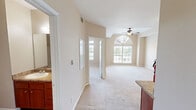 Located at 5300 S Lake Houston Pkwy in Houston, TX, this single-floor, one-bedroom, one-bathroom unit offers a well-organized layout comprising a bedroom, bathroom, kitchen, hallway, and closet. The bedroom is generously sized, featuring plush carpeting, a tray ceiling with crown molding, a ceiling fan with light fixture, and a large arched window that fills the room with natural light and offers views of the surrounding greenery. The living area showcases similar warm neutral tones, carpet flooring, and multiple vents for efficient climate control, with an electrical panel conveniently housed in the hallway. The kitchen is a functional highlight, outfitted with rich cherry-toned wood cabinetry, granite-style countertops, a stone tile backsplash, hardwood-style flooring, and black appliances including a refrigerator, electric range, dishwasher, and microwave. The bathroom continues the warm aesthetic with matching cherry wood cabinetry, granite-topped vanity, hardwood-style flooring, and a wall-mounted storage cabinet. Throughout, the unit maintains a cohesive, neutral color palette with beige walls and white trim, creating a clean and inviting atmosphere.