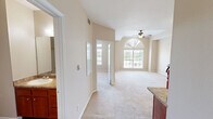 Located at 5300 S Lake Houston Pkwy in Houston, TX, this single-floor, one-bedroom, one-bathroom unit offers a well-organized layout comprising a bedroom, bathroom, kitchen, hallway, and closet. The bedroom is generously sized, featuring plush carpeting, a tray ceiling with crown molding, a ceiling fan with light fixture, and a large arched window that fills the room with natural light and offers views of the surrounding greenery. The living area showcases similar warm neutral tones, carpet flooring, and multiple vents for efficient climate control, with an electrical panel conveniently housed in the hallway. The kitchen is a functional highlight, outfitted with rich cherry-toned wood cabinetry, granite-style countertops, a stone tile backsplash, hardwood-style flooring, and black appliances including a refrigerator, electric range, dishwasher, and microwave. The bathroom continues the warm aesthetic with matching cherry wood cabinetry, granite-topped vanity, hardwood-style flooring, and a wall-mounted storage cabinet. Throughout, the unit maintains a cohesive, neutral color palette with beige walls and white trim, creating a clean and inviting atmosphere.