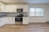 Located at 107 Wartburg Ave in Copiague, NY, this single-floor unit has been thoughtfully renovated with contemporary finishes and a clean, cohesive design. Light-toned hardwood flooring flows consistently throughout the space, complementing the neutral gray-white walls and bright white trim.

The kitchen is a standout feature, outfitted with crisp white shaker-style cabinetry, granite countertops, and a classic subway tile backsplash. A full suite of stainless steel GE appliances includes a refrigerator, gas range, over-the-range microwave, and dishwasher, providing a fully functional and modern cooking space. The kitchen opens toward a windowed dining or living area, allowing natural light to filter in through double-pane windows fitted with blinds.

The living areas are generously proportioned, offering an open and airy feel enhanced by the light flooring and neutral color palette. Baseboard heating units are present throughout, ensuring comfortable climate control. Additional rooms provide flexible living spaces, each featuring the same hardwood-style flooring and well-maintained finishes. The overall layout is practical and well-connected, with clear sightlines between rooms. The unit presents a clean, move-in-ready condition with a modern aesthetic suited for comfortable everyday living.