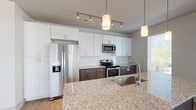 This single-floor residence at 2312 Bristol Creek Dr in Morrisville, NC offers a thoughtfully designed layout with modern finishes throughout. The kitchen is a standout feature, boasting granite countertops, a large center island with a undermount sink, two-tone cabinetry with white upper cabinets and dark lower cabinets, a classic subway tile backsplash, and stainless steel appliances including a refrigerator with ice maker, electric range, microwave, and dishwasher. Pendant and track lighting add a polished touch overhead. The open-concept layout connects the kitchen seamlessly to the living area, which features warm wood-look flooring and large windows that invite abundant natural light. The bedrooms are finished with plush carpeting, ceiling fans, and well-sized windows offering outdoor views. The primary bathroom features granite countertops, dark cabinetry, wood-look flooring, a glass-enclosed shower, and a walk-in closet. A secondary bathroom mirrors the same refined aesthetic with granite counters, dark cabinetry, and a tub-shower combination with marble-style tile surround. The neutral color palette and consistent finishes throughout create a cohesive, contemporary ambiance well-suited for comfortable everyday living.
