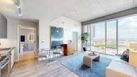 Located in the heart of Nashville's midtown neighborhood at 805 Church Street, this contemporary studio unit offers an efficient, thoughtfully designed single-floor layout. The combined living and dining area serves as the centerpiece of the space, anchored by dramatic floor-to-ceiling windows that flood the room with natural light and frame sweeping, unobstructed views of the Nashville downtown skyline. The open-concept design creates a seamless flow between the living, dining, and kitchen areas, with light hardwood flooring running throughout the main spaces. The kitchen features dark cabinetry with stainless steel appliances, including a refrigerator, microwave, and dishwasher, all accessible via a well-organized galley-style corridor. The sleeping area is quietly positioned away from the main living space, offering a built-in closet with shelving for ample storage. The full bathroom presents a clean, modern aesthetic with a backlit vanity mirror, sleek gray cabinetry, a white undermount sink, and a glass-enclosed shower. An in-unit laundry area and a dedicated entrance add further convenience. The overall ambiance is polished and contemporary, with neutral tones, high ceilings, and panoramic city views defining the character of this urban Nashville residence.