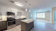 Located at 158–192 Wareham Rd in Plymouth, Massachusetts, this thoughtfully designed single-floor unit offers a contemporary living experience with high-quality finishes throughout. The open-concept kitchen serves as the heart of the home, anchored by a granite-topped center island with pendant lighting overhead. Two-tone cabinetry pairs white upper cabinets with warm wood-grain lower units, complemented by a full suite of stainless steel appliances including a gas range, microwave, dishwasher, and refrigerator. Light hardwood-style flooring flows seamlessly through the kitchen and main living areas, creating a bright and cohesive aesthetic. The living area benefits from generous natural light through large windows that frame views of the surrounding wooded landscape. Bedrooms feature plush carpeting, neutral soft-gray walls, ceiling fans, and windows with blinds that invite abundant daylight and outdoor greenery views. The primary bathroom offers a walk-in shower with grab bars, a granite-topped vanity with modern cabinetry, and light tile flooring. A second bathroom provides a full tub-shower combination, also equipped with accessibility grab bars and a matching granite vanity. The unit's clean, modern design and functional layout make it a well-rounded and comfortable living space.