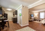 This single-floor residence in Peachtree Corners, Georgia, offers a thoughtfully designed layout with a cohesive neutral color palette and consistent finishes throughout. The living room serves as the central gathering space, featuring wood-look flooring, crown molding, and natural light admitted through blinded windows dressed with floor-length drape panels. The room comfortably accommodates a full seating arrangement centered around a glass-top coffee table.

The kitchen is equipped with dark espresso cabinetry, granite-style countertops, a stainless sink, and black appliances, all set atop warm hardwood-style flooring. Multiple bedrooms are carpeted and include ceiling fans, ample closet space—with at least one featuring a walk-in configuration—and windows that invite natural light. The rooms present a calm, restful atmosphere with neutral wall tones.

The bathrooms are consistently finished with dark vanity cabinetry, granite-style countertops, and wood-look tile flooring. Each includes a tub-shower combination with a decorative curtain. The overall design of the residence emphasizes practicality and visual cohesion, with matching finishes tying each room together into a unified and comfortable living environment.