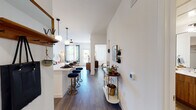This single-floor residence showcases a cohesive mid-century modern aesthetic carried throughout every room. The open-concept kitchen is a standout feature, outfitted with warm wood cabinetry, white subway tile backsplash, stainless steel appliances, and a central island with a white quartz countertop illuminated by globe pendant lights — ideal for both cooking and casual dining. Rich hardwood-style flooring flows seamlessly from the kitchen into the living and dining areas, creating a unified, expansive feel. The living room is bright and welcoming, benefiting from large windows that invite natural light, a ceiling fan overhead, and direct access to an outdoor area. A slim bar cart console along the hallway adds a functional and decorative touch to the transition between spaces. The bedroom is a calm retreat, featuring tall ceilings, generous windows with sheer curtains, a ceiling fan, and ample room for full-sized furniture. The bathroom is well-designed with a wide double-sink vanity featuring wood cabinetry, a large mirror, white subway tile surrounding the soaking tub and shower combination, and open shelving for storage. Throughout the residence, clean white walls, consistent flooring, and carefully considered lighting create a polished, livable environment with a warm, inviting ambiance.