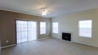 This single-floor residence offers a comfortable and well-appointed living environment designed with both functionality and style in mind. The living area serves as the heart of the space, featuring plush wall-to-wall carpeting that adds warmth underfoot. Crown molding frames the textured ceiling, lending a refined architectural detail to the room. A ceiling fan with integrated lighting provides both comfort and illumination, ensuring year-round comfort. Natural light floods the space through multiple windows fitted with horizontal blinds, as well as a sliding glass door that opens to a private balcony, offering an easy transition between indoor and outdoor living. The fireplace, framed by a clean white surround and hearth, serves as a striking focal point in the living area, perfect for creating a cozy ambiance. The neutral wall tones complement the light-colored trim and carpeting, resulting in a cohesive and inviting atmosphere throughout. The overall design is clean and understated, providing a versatile backdrop that accommodates a variety of interior styles and furnishing preferences.
