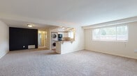Located at 8001 York Rd in Towson, Maryland, this single-floor residence offers a practical and functional layout designed for comfortable everyday living. The expansive main living area is finished with plush wall-to-wall carpeting and neutral white walls, creating a bright and open atmosphere. A large window allows natural light to pour in while offering views of the surrounding greenery. The kitchen is positioned at the heart of the home, defined by a convenient peninsula with a breakfast bar overhang. It features white cabinetry, dark laminate countertops, a stainless steel sink positioned beneath a window, and a black dishwasher. A stacked washer and dryer unit is neatly integrated into the kitchen space, providing the convenience of in-unit laundry. The bedroom areas are generously proportioned, with soft carpeting underfoot and an impressive amount of built-in storage, including dual closets with shelving and hanging rods. The bathroom includes wood-look flooring, a sliding glass shower enclosure, and a window for natural ventilation. An electrical panel is accessible within the living space, and the unit benefits from a dedicated entryway. Throughout, the clean, neutral palette offers a versatile canvas well-suited to a variety of furnishing styles.