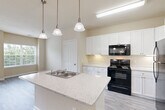 Located at 2001 Wood Hollow Place in Frederick, MD, this one-bedroom, one-bathroom residence offers a thoughtfully designed open-concept layout across a single floor. Light-toned walls, neutral-colored luxury vinyl plank flooring in the main living areas, and an abundance of natural light create a bright and welcoming ambiance throughout.

The combined kitchen and living room serves as the heart of the home. The well-appointed kitchen features a central island with a granite-style countertop, an undermount sink, and pendant lighting overhead. White shaker-style cabinetry provides generous storage, complemented by black appliances including an electric range, over-the-range microwave, and a full-size refrigerator. The living area flows naturally from the kitchen and opens to a private balcony through sliding glass doors, with an additional window allowing for ample natural light and outdoor views.

The generously sized bedroom is carpeted for comfort and includes a large window with views of the surrounding community. The full bathroom is finished with a white vanity, tile surround tub-shower combination, and coordinating flooring. The clean, neutral palette throughout the residence provides a versatile canvas adaptable to a variety of personal styles.