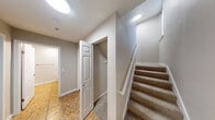 This three-floor space is thoughtfully designed with a consistent neutral color palette and a mix of flooring materials that distinguish each area's function. The kitchen serves as a standout feature, equipped with rich dark-wood cabinetry, white quartz countertops, stainless steel appliances including a range, microwave, and dishwasher, and a central island that provides additional prep and dining space. Wood-look flooring grounds the kitchen and flows cohesively through the main living areas.

The living room offers a welcoming focal point with a classic fireplace framed by a white mantel, complemented by warm hardwood flooring and track lighting overhead. Carpeted bedrooms provide a softer, quieter environment, each featuring vertical-blind windows that allow natural light while maintaining privacy, along with baseboard heating and ceiling light fixtures.

The bathroom includes a wide vanity with a white countertop, an undermount sink, dark wood cabinetry, tile flooring, and a walk-in shower with a glass enclosure and a large wall mirror.

A carpeted staircase connects the floors, while a hallway on the lower level features tile flooring and an open closet with built-in hanging storage, offering practical functionality throughout.