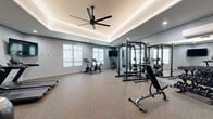 Located at 14378 Walnut Grove Way in Oregon City, Oregon, this dedicated fitness facility offers a generously sized, single-floor exercise room designed for a comprehensive workout experience. The room's most striking architectural feature is its elegant tray ceiling, accented with warm LED cove lighting and complemented by a large ceiling fan that ensures comfortable air circulation throughout the space. Recessed lighting adds to the bright, energizing atmosphere, while soft-toned gray walls and durable speckled rubber flooring create a clean, modern aesthetic.

The space is thoughtfully organized to accommodate a wide variety of training disciplines. The cardio zone features two treadmills, a stationary spin bike, and an elliptical machine, all positioned beneath a wall-mounted flat-screen television. A dedicated strength training area includes a power rack with attached weight storage, a cable machine, an adjustable bench, and a full rack of dumbbells — all reflected in floor-to-ceiling mirrors that enhance the sense of space. A TRX functional training station is wall-mounted and stocked with kettlebells, medicine balls, and resistance accessories. Natural light filters in through frosted windows, and the room is accessible via a double-door entry, rounding out this well-appointed fitness space.