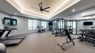 Located at 14378 Walnut Grove Way in Oregon City, Oregon, this dedicated fitness facility offers a generously sized, single-floor exercise room designed for a comprehensive workout experience. The room's most striking architectural feature is its elegant tray ceiling, accented with warm LED cove lighting and complemented by a large ceiling fan that ensures comfortable air circulation throughout the space. Recessed lighting adds to the bright, energizing atmosphere, while soft-toned gray walls and durable speckled rubber flooring create a clean, modern aesthetic.

The space is thoughtfully organized to accommodate a wide variety of training disciplines. The cardio zone features two treadmills, a stationary spin bike, and an elliptical machine, all positioned beneath a wall-mounted flat-screen television. A dedicated strength training area includes a power rack with attached weight storage, a cable machine, an adjustable bench, and a full rack of dumbbells — all reflected in floor-to-ceiling mirrors that enhance the sense of space. A TRX functional training station is wall-mounted and stocked with kettlebells, medicine balls, and resistance accessories. Natural light filters in through frosted windows, and the room is accessible via a double-door entry, rounding out this well-appointed fitness space.