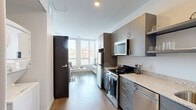 Located at 120 20th Ave S in Nashville's vibrant Midtown neighborhood, this modern 2-bedroom, 3-bathroom residence offers a thoughtfully designed single-floor layout. The galley-style kitchen is outfitted with stainless steel appliances including a range, dishwasher, and over-the-range microwave, complemented by granite countertops, gray cabinetry, open floating shelves, and warm wood-look flooring that flows throughout the unit. A large window at the end of the kitchen draws in natural light and provides neighborhood views. Each bedroom is bright and efficiently proportioned, featuring large windows with slatted blinds, individual wall-mounted HVAC units, and access to closet storage. The primary bedroom includes its own dedicated closet and en-suite bathroom. The three bathrooms maintain a consistent modern aesthetic, each featuring gray vanity cabinetry with granite countertops, a large mirror, and clean white finishes. A stacked in-unit washer and dryer adds everyday convenience. Crisp white walls, dark-framed doors, and consistent wood-look flooring unify the space with a clean, contemporary feel throughout.