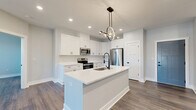 Located at 4405 River Creek Rd in Kings Mills, Ohio, this well-appointed single-floor home offers three bedrooms, two bathrooms, and a thoughtfully designed open-concept layout. The combined kitchen and living area serves as the heart of the home, featuring rich wood-tone flooring, recessed lighting, and a ceiling fan that enhance the bright, airy atmosphere. French doors lead to a private balcony, allowing natural light to pour in while providing outdoor access.

The kitchen is a standout feature, showcasing crisp white shaker cabinetry, white quartz countertops, a large center island with a sink, and stainless steel appliances including a refrigerator, range, and over-the-range microwave. A modern circular pendant light adds a contemporary design touch above the island.

The bedrooms are well-sized, each finished with the same durable wood-tone flooring, neutral soft-gray walls, and large windows that invite natural light. The generously sized primary bedroom offers comfortable living space. The bathrooms are clean and simply appointed with white vanities and matching finishes throughout.

Storage is plentiful, with six closets across the home, including walk-in closets fitted with wire shelving systems. A dedicated utility room rounds out the functional layout of this move-in-ready home.