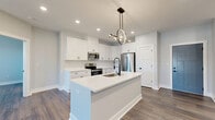 Located at 4405 River Creek Rd in Kings Mills, Ohio, this well-appointed single-floor home offers three bedrooms, two bathrooms, and a thoughtfully designed open-concept layout. The combined kitchen and living area serves as the heart of the home, featuring rich wood-tone flooring, recessed lighting, and a ceiling fan that enhance the bright, airy atmosphere. French doors lead to a private balcony, allowing natural light to pour in while providing outdoor access.

The kitchen is a standout feature, showcasing crisp white shaker cabinetry, white quartz countertops, a large center island with a sink, and stainless steel appliances including a refrigerator, range, and over-the-range microwave. A modern circular pendant light adds a contemporary design touch above the island.

The bedrooms are well-sized, each finished with the same durable wood-tone flooring, neutral soft-gray walls, and large windows that invite natural light. The generously sized primary bedroom offers comfortable living space. The bathrooms are clean and simply appointed with white vanities and matching finishes throughout.

Storage is plentiful, with six closets across the home, including walk-in closets fitted with wire shelving systems. A dedicated utility room rounds out the functional layout of this move-in-ready home.