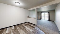 Unit #208 at 3 Falls in Sioux Falls, South Dakota is a well-organized one-bedroom, one-bathroom residence spread across a single floor. The layout flows efficiently from a welcoming hallway into the main living areas, with distinct flooring transitions helping to define each space — wood-look vinyl planks in the common areas and kitchen, and plush carpet in the bedroom and living room.

The galley-style kitchen is thoughtfully appointed with dual-toned cabinetry — white upper cabinets on one side and warm wood-toned lower cabinets on the other — complemented by dark laminate countertops, a double-basin sink, and a full suite of white appliances including a range, dishwasher, and refrigerator. A textured ceiling adds classic character throughout.

The bedroom is a comfortable, well-proportioned retreat featuring neutral carpeting, a ceiling fan with light fixture, a window that allows natural light, and baseboard heating. The clean, neutral wall tones create a calm and versatile backdrop.

The bathroom is outfitted with a full-sized soaking tub and shower combo with crisp white surround panels and polished chrome fixtures. A pass-through shelf detail in the living area adds a subtle architectural touch, while a sliding glass door opens to an outdoor balcony, bringing in additional natural light and providing outdoor access.