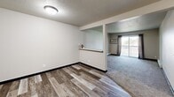 Unit #208 at 3 Falls in Sioux Falls, South Dakota is a well-organized one-bedroom, one-bathroom residence spread across a single floor. The layout flows efficiently from a welcoming hallway into the main living areas, with distinct flooring transitions helping to define each space — wood-look vinyl planks in the common areas and kitchen, and plush carpet in the bedroom and living room.

The galley-style kitchen is thoughtfully appointed with dual-toned cabinetry — white upper cabinets on one side and warm wood-toned lower cabinets on the other — complemented by dark laminate countertops, a double-basin sink, and a full suite of white appliances including a range, dishwasher, and refrigerator. A textured ceiling adds classic character throughout.

The bedroom is a comfortable, well-proportioned retreat featuring neutral carpeting, a ceiling fan with light fixture, a window that allows natural light, and baseboard heating. The clean, neutral wall tones create a calm and versatile backdrop.

The bathroom is outfitted with a full-sized soaking tub and shower combo with crisp white surround panels and polished chrome fixtures. A pass-through shelf detail in the living area adds a subtle architectural touch, while a sliding glass door opens to an outdoor balcony, bringing in additional natural light and providing outdoor access.