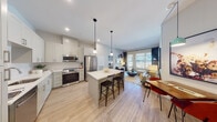 This contemporary single-floor residence offers a thoughtfully designed open-concept layout that seamlessly integrates the kitchen, dining, and living areas into one cohesive and functional space. The kitchen is a standout feature, equipped with stainless steel appliances including a French door refrigerator, range, and built-in microwave, all complemented by crisp white shaker cabinetry, quartz countertops, a textured tile backsplash, and a central island with bar seating. Pendant lighting adds a refined touch overhead, while light wood-tone flooring flows continuously throughout the residence. The living area is bright and welcoming, benefiting from large windows and a glass door that opens to a private balcony, offering views of the surrounding community. Two bedrooms provide comfortable retreats; the primary bedroom features a large window with sheer drapery, while the secondary bedroom offers a cozy, versatile layout. The bathrooms are finished with clean, modern details, including a backlit vanity mirror, white quartz countertops, shaker-style cabinetry, and wood-look tile flooring. A hallway with closet space connects the private areas of the residence. The overall ambiance is light, airy, and contemporary throughout.