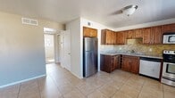This single-story, 2-bedroom, 1-bathroom home offers a practical and comfortable layout across one level. The combined kitchen and living area serves as the heart of the home, featuring warm-toned ceramic tile flooring and a well-equipped kitchen outfitted with rich walnut-stained wood cabinetry, granite countertops, a stone mosaic tile backsplash, a built-in wine rack, and a full suite of stainless steel appliances including a refrigerator, range, microwave, and dishwasher. Natural light filters in through a window adjacent to the kitchen, enhancing the brightness of the space. The living area provides an open, airy feel with neutral walls and tile flooring that flows seamlessly from the kitchen. The two bedrooms are carpeted and offer ceiling fans for added comfort. The primary bedroom features a sliding glass door with vertical blinds that allows natural light and outdoor access, while the second bedroom maintains a cozy, neutral aesthetic. A hallway connects the main living spaces to the full bathroom, which includes tile flooring, a granite-topped vanity with dark wood cabinetry, and a tub/shower combination with full-height travertine-style tile surround.