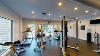 Located at 455 Arbor Pl in Nashville, Tennessee, this well-equipped fitness center is designed to support a comprehensive workout experience on a single level. The facility is divided into two distinct zones, each tailored to a specific type of training.

The cardio area is bright and inviting, featuring large windows on multiple walls that flood the space with natural light and offer views of the surrounding outdoor greenery. Recessed lighting complements the natural light overhead. This section is outfitted with a variety of cardio machines, including treadmills, ellipticals, upright and recumbent bikes, and a stair climber, all positioned to take advantage of the window views. A wall-mounted TV bracket is also present for entertainment.

The strength and functional training area has a more industrial aesthetic, with exposed ductwork along the ceiling and accent walls in green and gray tones. This section houses a Smith machine with free weights and a bench, a cable crossover machine, a dumbbell rack, and an extensive collection of medicine balls and stability balls organized on dedicated storage racks. Resistance bands and a TRX-style suspension training system round out the functional training options. A water cooler and informational board are also available. Dark rubber flooring throughout both zones provides durability and safety, and a glass door with sidelight offers direct outdoor access.