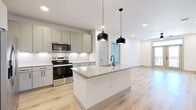 This well-appointed 2-bedroom, 2-bathroom residence is thoughtfully designed across a single floor, offering a cohesive and functional layout. The open-concept kitchen and living area serves as the heart of the home, featuring a central island with a granite countertop and an integrated sink, illuminated by a pair of striking matte black pendant lights. The kitchen is outfitted with gray flat-panel cabinetry, stainless steel appliances including a range, microwave, and refrigerator, and a textured tile backsplash that adds dimension to the clean design. Light wood-tone flooring flows throughout the main living areas, complementing the bright white walls and recessed lighting overhead. A built-in desk nook with matching cabinetry provides a dedicated workspace off the kitchen. The bedrooms are carpeted for comfort and feature ceiling fans, generous windows that invite natural light and outdoor views, and access to well-organized walk-in closets with built-in shelving and hanging rods. The primary bathroom includes a granite-topped vanity with gray cabinetry, a soaking tub with tiled surround, wood-look flooring, and matte black hardware throughout. A sliding barn-style door adds a modern architectural touch. The space is finished with a neutral, contemporary palette throughout.