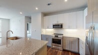 This single-floor residence showcases a contemporary design with a thoughtful layout and high-quality finishes throughout. The kitchen serves as a central highlight, featuring a large granite-topped island with an undermount sink, white upper cabinetry paired with textured gray lower cabinets, a white subway tile backsplash, and a full suite of stainless steel appliances including a range, over-the-range microwave, and French door refrigerator. Rich hardwood flooring runs throughout the main living and kitchen areas, complementing the clean, modern aesthetic.

The living area benefits from expansive floor-to-ceiling windows that invite abundant natural light and offer elevated views of the surrounding urban landscape. Recessed lighting throughout provides additional illumination in each space.

The bedrooms are carpeted for comfort and each include ceiling fans and windows with roller shades that overlook neighboring buildings. Two full bathrooms are present in the unit. The primary bathroom features a dual-sink vanity with granite countertops, a large wall mirror, a soaking tub, a separate walk-in shower, and direct access to a carpeted walk-in closet. A second bathroom also includes granite countertops, a glass-enclosed shower, and its own walk-in closet access, maintaining consistent finishes throughout.
