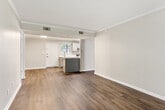 This single-story unit offers a thoughtfully designed layout across two bedrooms and three bathrooms. The open-concept kitchen flows seamlessly into the living area, creating a cohesive and functional space. The kitchen is outfitted with gray shaker-style cabinetry, white quartz countertops, a subway tile backsplash, stainless steel appliances including a range, dishwasher, and refrigerator, and a single-basin sink positioned near a window for natural light.

The living room extends toward a set of French doors that invite natural light and provide outdoor access, adding an airy quality to the space. Neutral gray walls, crown molding, and dark hardwood-style flooring are consistent throughout the main living areas, contributing to a clean, contemporary aesthetic.

The primary bedroom is a comfortable size, featuring its own dedicated closet and an en-suite bathroom. The bathroom includes an extended gray vanity with white quartz countertops, brushed nickel fixtures, a framed mirror, and a separate tiled tub-shower combination. The second bedroom includes a window with outdoor views. A walk-in closet with multi-tier shelving provides ample storage. The textured ceilings are present in select areas of the unit.