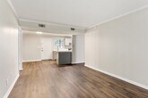 This single-story unit offers a thoughtfully designed layout across two bedrooms and three bathrooms. The open-concept kitchen flows seamlessly into the living area, creating a cohesive and functional space. The kitchen is outfitted with gray shaker-style cabinetry, white quartz countertops, a subway tile backsplash, stainless steel appliances including a range, dishwasher, and refrigerator, and a single-basin sink positioned near a window for natural light.

The living room extends toward a set of French doors that invite natural light and provide outdoor access, adding an airy quality to the space. Neutral gray walls, crown molding, and dark hardwood-style flooring are consistent throughout the main living areas, contributing to a clean, contemporary aesthetic.

The primary bedroom is a comfortable size, featuring its own dedicated closet and an en-suite bathroom. The bathroom includes an extended gray vanity with white quartz countertops, brushed nickel fixtures, a framed mirror, and a separate tiled tub-shower combination. The second bedroom includes a window with outdoor views. A walk-in closet with multi-tier shelving provides ample storage. The textured ceilings are present in select areas of the unit.