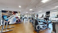 Located at 26 Belden Ave in Norwalk, Connecticut, this fitness center offers a spacious, single-floor layout designed to accommodate a full range of workout activities. The facility features warm hardwood-style flooring throughout, a drop ceiling with recessed and panel lighting, and large windows along the perimeter that allow natural light to fill the space and provide views of the surrounding area.

The cardio zone is well-stocked with treadmills, elliptical trainers, stationary bikes, and rowing machines, many equipped with individual monitor screens. A dedicated strength-training area includes a multi-station cable machine, a comprehensive dumbbell rack, and various benches and resistance machines suitable for both upper and lower body workouts. Mirrors are positioned strategically to support proper form during exercises.

Motivational large-scale wall murals featuring athletes in action are displayed prominently throughout the space, reinforcing an energetic and encouraging atmosphere. A stretching and functional fitness area provides open floor space along with built-in storage cubbies, offering room for cool-downs and flexibility work. The overall ambiance is clean, bright, and professionally designed, making this fitness center a fully functional destination for a wide variety of training needs.