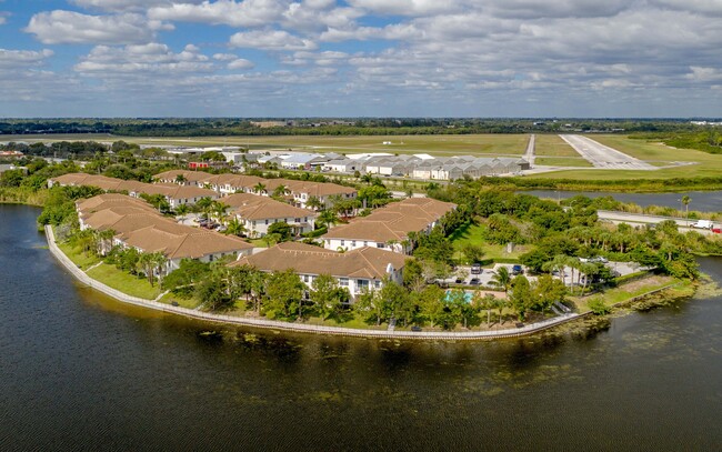 Aerial view of elegant lakeside apartments with charming terracotta roofs surrounded by lush greenery and scenic water views, enhancing a serene lifestyle. - Bridgewater at Lake Osborne