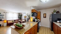 This two-floor residence offers a well-designed layout that balances comfort and functionality throughout. The living room serves as a welcoming centerpiece, featuring light wood-style flooring, a large sectional sofa, and an abundance of natural light complemented by lush indoor greenery. A full-length decorative mirror and contemporary wall art add visual depth to the space.

The kitchen is outfitted with warm wood cabinetry, granite countertops, stainless steel appliances including a refrigerator, electric range, built-in microwave, and dishwasher. A central island with a double sink flows seamlessly into the adjacent dining area, which features hardwood-style flooring, a pendant chandelier, and a large window dressed with sheer curtains.

The bedrooms are carpeted for warmth and comfort, each equipped with ceiling fans and ample closet space. The primary bedroom offers generous proportions with soft neutral tones and well-sized windows. A second bedroom provides a cozy retreat with similar finishes and bright natural light.

The bathrooms include a half bath with granite vanity and light wood flooring, as well as a full bath featuring a tub-shower combination with white tile surround. Throughout the home, consistent warm-toned finishes and wood cabinetry create a cohesive and inviting atmosphere.