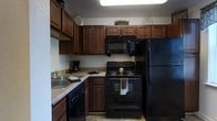 This two-floor residence offers a practical and well-appointed living environment. The kitchen is a standout feature, showcasing rich, dark-stained wood cabinetry that extends to the upper walls, providing generous storage space. The cabinetry's raised-panel doors add a traditional character to the room. A full suite of black appliances includes a gas range with oven, over-the-range microwave, dishwasher, and a full-sized refrigerator, creating a cohesive and functional cooking space. The countertops offer ample prep surface area, and a stainless steel sink is positioned conveniently along the perimeter. Tile flooring runs throughout the kitchen, adding durability and ease of maintenance. The interior doors throughout the residence are white with a classic single raised-panel design, fitted with brass-toned lever and deadbolt hardware, contributing to a traditional aesthetic. The neutral wall tones and consistent design language across the space create a cohesive and inviting atmosphere. Spanning two floors, the layout offers a natural separation between living and private areas, providing both functionality and comfort for everyday living.