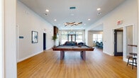 Located at 700 N 40th St in Rogers, Arkansas, this contemporary single-floor community clubhouse delivers a well-rounded amenity experience across a generously sized footprint. The space is defined by clean white walls, warm light wood flooring, and an abundance of natural light streaming through large black-framed floor-to-ceiling windows and glass doors.

The central gathering area serves as the heart of the clubhouse, anchored by a full-size billiards table beneath a striking geometric chandelier. Adjacent to it, a comfortable lounge features leather seating, a fireplace with a wood-slat accent wall, and sweeping views of the outdoor pool area through expansive glass walls, seamlessly connecting indoor and outdoor living.

The fully equipped kitchen showcases gray shaker cabinetry, white quartz countertops, a large center island with bar seating, stainless steel appliances, and a decorative mosaic tile backsplash—ideal for community events and gatherings.

Two private conference rooms offer a focused work environment, each furnished with a table, upholstered chairs, a wall-mounted display, and natural light from exterior-facing windows. A dedicated parcel locker room with floor-to-ceiling smart lockers provides secure package retrieval. The entryway features tall ceilings, curated artwork, and a parcel room access point, rounding out this thoughtfully designed community space.