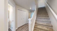 This two-story home is designed with a clean, contemporary aesthetic and a practical layout spread across two levels. The main level showcases a well-appointed kitchen as its centerpiece, featuring crisp white shaker-style cabinetry, dark granite countertops, and a full suite of stainless steel appliances including a refrigerator, electric range, and over-the-range microwave. A central island with a undermount sink and pendant lighting above adds both functionality and visual interest. Light hardwood-style flooring flows throughout the main level, contributing to a bright, cohesive feel.

The upper level is accessed via a carpeted staircase with a classic white banister and newel post. At the top of the stairs, an open loft area provides flexible living space illuminated by recessed lighting. Bedrooms on this floor feature plush carpeting, neutral walls, and windows that allow natural light to filter in. A full bathroom serves the upper level, finished with a single-sink vanity, white countertop, and a tub-shower combination with chrome fixtures and hardwood-style tile flooring.

Additional storage is available through a large double-door closet on the lower level. The attached two-car garage offers generous space with a concrete floor, drywalled walls, and an automatic garage door opener.