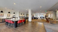 Located at 1550 Raleigh St in Denver's vibrant West Colfax neighborhood, this single-floor amenity space delivers a dynamic and modern environment designed for both social interaction and productive work. The layout flows across several distinct yet interconnected zones, all unified by warm hardwood-style flooring, recessed lighting, and large floor-to-ceiling windows that invite abundant natural light and outdoor views.

The main clubroom is a spacious, open-plan gathering area featuring a bold bar-height communal table with red chairs, pendant lighting, and a striped lounge booth. A billiards table anchors the game zone nearby, adding a recreational focal point. Adjacent to this is a comfortable lounge area furnished with plush sofas, accent chairs, a wall-mounted TV, and curated artwork, complemented by a tile-surround fireplace and direct access to an outdoor area.

The lobby and mail center area showcases a striking teal accent wall, a large built-in mailbox bank, terrazzo flooring, and an oversized island counter beneath geometric pendant lights. Decorative textured panels with colorful accents add visual interest throughout.

A dedicated conference room offers a large dark wood table, rolling chairs, a wall-mounted display, and views toward the street entrance — ideal for meetings or private gatherings. The overall ambiance is contemporary, welcoming, and thoughtfully designed for community living.