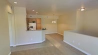 This two-floor residential space offers a well-designed, open-concept layout that promotes a seamless flow between the primary living areas. The main floor centers around a bright, connected kitchen and dining area. The kitchen features warm wood cabinetry, a granite-topped peninsula that doubles as a breakfast bar, recessed lighting, and a full suite of appliances including a refrigerator. The peninsula creates a natural divide between the kitchen and the adjoining living area, while maintaining the open feel of the space. The dining area is illuminated by a classic chandelier, adding a welcoming touch to the room. Neutral, light-toned walls run throughout, giving the space a clean and airy ambiance. The flooring transitions between smooth hard surface near the kitchen and plush carpeting in the living and dining zones, providing both practicality and comfort. Recessed lighting and HVAC vents are integrated into the ceiling, ensuring comfort throughout. The second floor extends the living space further, offering additional rooms accessible from the main level. Overall, the space combines functional design with a warm, approachable aesthetic suited for everyday living.
