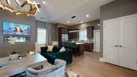 Located at 226 Dorchester Dr in Princeton Junction, NJ, this single-floor amenity space combines contemporary design with functional comfort. The entry foyer features crisp white board-and-batten wall paneling and a glass-paned French door, setting an elegant tone from the moment of arrival.

The spacious open-concept lounge area is a standout feature, anchored by a striking geometric gold chandelier suspended from elevated ceilings with detailed crown molding. Warm gray walls and white wainscoting create a refined backdrop for plush emerald green velvet seating and coordinating swivel chairs. A wall-mounted flat-screen television sits above a sleek linear fireplace framed in large-format tile, while natural light filters through multiple windows dressed with tailored drapery panels.

Flowing directly from the lounge, the full kitchen is equipped with rich dark espresso cabinetry, white quartz countertops, stainless steel appliances, and a decorative tile backsplash. A center island with emerald green bar seating provides additional gathering space, with pendant lighting overhead.

The fitness center offers a well-equipped workout environment featuring treadmills, ellipticals, free weights, wall-to-wall mirrors, dark rubberized flooring, and wall-mounted televisions — all bathed in natural light.
