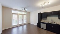 This well-appointed single-floor unit offers a thoughtfully designed open-concept layout that seamlessly connects the kitchen and living areas. The kitchen is a standout feature, boasting sleek dark cabinetry paired with granite countertops, a tile backsplash, and a full suite of stainless steel appliances including a refrigerator, range, built-in microwave, and dishwasher. Track lighting above the kitchen provides focused illumination, complementing the warm wood-look flooring that runs throughout the main living area.

The spacious living area is bathed in natural light, thanks to a set of full-height French doors that open onto a private balcony with outdoor views. A ceiling fan enhances comfort and airflow within the open space. The layout also includes a generously sized bedroom with neutral tones and ample wall space, providing a versatile and restful retreat.

The bathroom is finished with the same attention to detail found throughout the unit, featuring a granite-topped dark vanity, a large framed mirror, brushed nickel fixtures, and a full tub-shower combination with tiled surround. Clean lines and a neutral color palette throughout create a cohesive, modern aesthetic that is both functional and inviting.