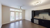 This well-appointed single-floor unit offers a thoughtfully designed open-concept layout that seamlessly connects the kitchen and living areas. The kitchen is a standout feature, boasting sleek dark cabinetry paired with granite countertops, a tile backsplash, and a full suite of stainless steel appliances including a refrigerator, range, built-in microwave, and dishwasher. Track lighting above the kitchen provides focused illumination, complementing the warm wood-look flooring that runs throughout the main living area.

The spacious living area is bathed in natural light, thanks to a set of full-height French doors that open onto a private balcony with outdoor views. A ceiling fan enhances comfort and airflow within the open space. The layout also includes a generously sized bedroom with neutral tones and ample wall space, providing a versatile and restful retreat.

The bathroom is finished with the same attention to detail found throughout the unit, featuring a granite-topped dark vanity, a large framed mirror, brushed nickel fixtures, and a full tub-shower combination with tiled surround. Clean lines and a neutral color palette throughout create a cohesive, modern aesthetic that is both functional and inviting.