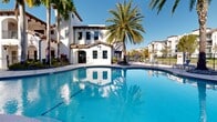 This upscale residential complex in Doral, Florida, showcases a stunning blend of Mediterranean and tropical aesthetics. The property boasts multiple expansive swimming pools, each surrounded by pristine decking and comfortable lounge chairs. The pools' unique shapes and sizes create a resort-like atmosphere, with some featuring curved edges and others offering lap lanes for exercise.

The architecture is characterized by its white stucco exterior, red tile roofs, and elegant arched entryways, reminiscent of Mediterranean villas. Multi-story buildings with private balconies overlook the meticulously landscaped grounds. Palm trees of various species, including royal palms and date palms, line the walkways and pool areas, providing natural shade and a lush tropical ambiance.

Amenities include covered outdoor seating areas with pillared structures, perfect for relaxation or social gatherings. The complex also features well-maintained gardens with vibrant red flowers and green shrubbery, enhancing the overall aesthetic appeal.

The property's design emphasizes outdoor living and community spaces, with ample seating areas and open green spaces. The combination of crystal-clear pools, verdant landscaping, and elegant architecture creates a serene and luxurious environment for residents to enjoy the Florida sunshine year-round.