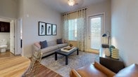 Located in Fredericksburg, VA, this single-floor residence offers a thoughtfully designed layout with two bedrooms, two bathrooms, and a well-equipped kitchen. The kitchen is a standout feature, showcasing rich dark cabinetry, mosaic tile backsplash, stainless steel appliances including a refrigerator, range, and microwave, white quartz countertops, and warm hardwood-style flooring. A spacious island with seating provides an ideal spot for casual dining, complemented by pendant lighting above. The living area is bright and welcoming, featuring hardwood-style flooring, large windows with decorative curtains, and direct access to an outdoor area via a glass panel door. The primary bedroom is generously sized with plush carpeting, large windows that invite natural light, and an en-suite bathroom featuring a dual-sink vanity with dark cabinetry, white countertops, a glass-enclosed walk-in shower, and access to a spacious walk-in closet with wire shelving. The second bedroom is cozy and well-lit, also featuring carpeted flooring and ample natural light. The second bathroom includes a single-sink vanity, a tub-shower combination, and convenient closet access. Throughout, the neutral color palette and modern finishes create a clean, cohesive aesthetic.