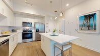 Located at 3680 46th Ave S in Saint Petersburg, Florida, this single-floor residence offers a thoughtfully designed open-concept layout with modern coastal aesthetics. The kitchen is a standout feature, showcasing sleek white cabinetry extending to the ceiling, a subway tile backsplash, stainless steel appliances including a French door refrigerator, range, and built-in microwave, and a large white quartz island with bar seating illuminated by elegant pendant lighting. Light wood-tone flooring flows throughout the main living areas, enhancing the bright and airy atmosphere. The living room is bathed in natural light from floor-to-ceiling sliding glass doors that open to an outdoor area, complemented by a ceiling fan and a relaxed coastal-inspired ambiance. The bedrooms are comfortably scaled, featuring plush carpeting, natural light from windows with stylish window treatments, and a calming neutral palette. The primary bedroom is served by a well-appointed full bathroom with a soaking tub and shower combination, and a generous walk-in closet with wire shelving. A second walk-in closet provides additional storage. Clean lines, recessed and track lighting, and a cohesive white-and-neutral color scheme give the entire space a fresh, contemporary feel suited to Florida living.