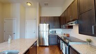 Located at 400 Belmont, this single-floor residence offers a thoughtfully designed layout with a cohesive blend of modern finishes and practical amenities. The kitchen serves as a standout feature, showcasing rich dark-stained cabinetry that extends to ceiling height, granite countertops, a classic white subway tile backsplash, and a full suite of stainless steel appliances including a refrigerator, range, and built-in microwave. A generously sized kitchen island with a granite surface and an integrated sink adds both prep space and visual interest, anchoring the open flow between the kitchen and living areas. Warm hardwood-style flooring runs throughout the main living spaces, complementing the neutral wall tones and contributing to an inviting ambiance. The living area benefits from natural light through large windows and a French door entry, with a ceiling fan adding comfort. A dedicated laundry area with a washer and dryer is conveniently accessible. The bathroom features a tub-shower combination with grab bars and dark vanity cabinetry with granite counters. The bedroom offers plush carpeting and a large window with outdoor views, creating a bright, comfortable retreat.
