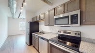 This studio in Memphis, TN offers a thoughtfully designed single-floor layout that efficiently combines living and kitchen functions within a compact yet functional footprint. The open-concept kitchen and living area is defined by an industrial aesthetic, highlighted by exposed metallic ductwork running along the ceiling and black track lighting that provides both ambient and directional illumination. Light hardwood-style flooring extends throughout the entire unit, contributing to a clean, cohesive look.

The kitchen is well-appointed with dark taupe cabinetry, granite-style countertops, and a full suite of stainless steel appliances, including a refrigerator, electric range, built-in microwave, and dishwasher. The living area benefits from a row of windows along one wall, allowing natural light to fill the space, complemented by a blue accent wall that adds a touch of visual character.

The bathroom features a granite-topped vanity with wood cabinetry, a large mirror, and hardwood-style flooring consistent with the rest of the unit. A dedicated laundry area includes a full-size GE top-loading washer and dryer alongside wire shelving for additional storage. Overall, the space presents a modern, urban aesthetic suited for efficient single-occupant living.