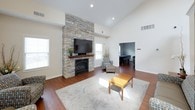This single-floor community space is thoughtfully designed to offer a variety of functional areas within an open, airy layout. The centerpiece of the main lounge is a striking floor-to-ceiling stacked stone fireplace with a wood mantel, topped by a wall-mounted television, creating a warm and inviting focal point. Soaring vaulted ceilings amplify the sense of openness throughout, while rich hardwood flooring runs continuously across the space. Multiple windows allow natural light to pour in, enhancing the bright, neutral color palette.

The fully equipped kitchen features warm-toned wood cabinetry, granite countertops, black appliances including a gas range, microwave, and refrigerator, and a generous island that provides ample prep and serving space. An adjacent seating area with armchairs and accent décor offers a comfortable space to relax.

A dedicated game room, visible from the main lounge, is furnished with a pool table and casual seating, making it ideal for recreational use. A separate workspace area provides a desk and television, catering to those who need a quiet area for individual tasks. Throughout the space, the combination of high ceilings, natural light, and thoughtful furnishings creates an inviting and versatile environment suited for a range of activities and gatherings.