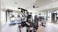 Located at 777 Dunlavy St in Houston's 77019 zip code, this fitness center offers a thoughtfully designed exercise space optimized for a comprehensive workout experience. The room is finished with neutral-toned flooring and soft sage-green walls, creating a clean, modern aesthetic that promotes focus and energy.

Large windows line the perimeter, flooding the space with abundant natural light and offering views of the surrounding urban environment. Full-length mirrors are strategically mounted along the walls, enhancing the sense of openness and allowing users to monitor their form. A ceiling fan provides additional climate comfort overhead.

The exercise room is well-appointed with a diverse selection of equipment to support both cardio and strength training. Cardio offerings include multiple Star Trac treadmills and elliptical machines, while the strength training section features a multi-station cable machine, selectorized weight machines, a free weight rack with a full set of dumbbells, and adjustable workout benches. A glass partition wall visually connects the fitness area to an adjacent space, adding depth and transparency to the layout.

The combination of ample natural light, mirrored walls, modern equipment, and an open floor plan makes this fitness center a functional and inviting space for a wide range of workout routines.