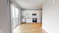 Located at 940 E Adams St in Jacksonville, Florida, this single-floor unit offers a thoughtfully designed layout that maximizes functionality and comfort. The open-concept living and kitchen area is highlighted by warm light hardwood flooring, creating a bright and welcoming atmosphere. The modern kitchen is a standout feature, equipped with sleek white cabinetry, a classic subway tile backsplash, stainless steel appliances including a refrigerator, range, microwave, and dishwasher, and a single-basin sink. Track lighting overhead ensures the space is well-lit, while large windows allow natural light to filter in. A ceiling fan is centrally positioned in the main living area, promoting comfortable airflow throughout. The bedroom is finished with soft wall-to-wall carpeting underfoot and features its own ceiling fan, a sliding closet door for efficient space use, and windows fitted with blinds for privacy and light control. Neutral gray-toned walls throughout the unit lend a clean, contemporary aesthetic that pairs well with the varied flooring materials. A hallway connects the main living areas, contributing to a smooth and practical flow within the space.