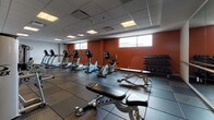 Located at 18 Front St. within 81 Arch's in Hartford, CT, this single-floor fitness center offers a well-equipped and thoughtfully designed space for comprehensive workouts. The gym features durable rubber tile flooring in a classic checkerboard pattern, providing both safety and easy maintenance throughout the facility. A suspended drop ceiling with recessed panel lighting ensures consistent, even illumination across the entire floor.

The cardio zone is stocked with a variety of TRUE and Cybex machines, including treadmills, ellipticals, upright and recumbent bikes, and rowing equipment, arranged to allow comfortable spacing between users. The strength training area features a full dumbbell rack with a wide range of weights, a Hoist adjustable weight bench, and multiple selectorized cable and resistance machines by Cybex.

A dedicated functional training corner includes a rack of medicine balls in various weights, a BOSU balance trainer, and a wall-mounted exercise mat, complemented by a large flat-screen TV. A wall of mirrors paired with a ballet barre adds a studio element, making the space suitable for stretching and balance work. The accent wall, painted in a bold terra cotta, is adorned with an inspiring typographic mural reading "Eat Well, Move Daily, Hydrate Often, Sleep Lots, Love Yourself, Repeat for Life," setting an energizing tone throughout the facility.