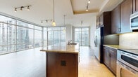 Located in the heart of downtown Austin at 101 Colorado St, this two-bedroom, one-bathroom residence offers an impressive high-rise living experience with panoramic views of the city skyline and the waterway below. The open-concept living, dining, and kitchen area is anchored by dramatic floor-to-ceiling glass windows that flood the space with natural light and frame breathtaking views of Austin's urban landscape. The kitchen is equipped with rich dark wood cabinetry reaching to the ceiling, stainless steel appliances including a double oven and refrigerator, a granite-topped center island with a built-in sink, and elegant tile flooring. The living area features wide-plank wood flooring that extends throughout the bedrooms, lending warmth and continuity to the space. A private balcony provides direct access to sweeping outdoor views of the downtown skyline. Both bedrooms are well-proportioned, with the primary bedroom offering particularly generous dimensions. The space includes three closets — one of which is a spacious walk-in with wire shelving — providing ample storage. A built-in desk nook with shelving adds functional versatility. The bathroom is finished with travertine tile, a dark wood vanity, and a full soaking tub with tiled surround. A dedicated laundry area completes this well-appointed downtown Austin residence.