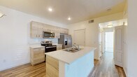 This well-designed single-floor residence showcases a clean, contemporary aesthetic throughout. The heart of the home is an open-concept kitchen that impresses with light wood cabinetry, white quartz countertops, a subway tile backsplash, and a full suite of stainless steel appliances including a range, over-the-range microwave, and a French door refrigerator. A central island with an integrated sink adds functional prep space and serves as a natural gathering point, while a pendant light overhead adds a warm finishing touch. Wood-look flooring extends seamlessly through the kitchen and living areas, lending a cohesive, modern feel. The living area is bright and open, highlighted by French doors that invite natural light and provide access to the outdoors. The bedrooms feature soft, neutral carpet and windows fitted with blinds, creating calm and comfortable retreats. Each bedroom includes closet space, with at least one offering a dedicated closet with rod and shelving. The two bathrooms are finished in a consistent style, featuring light wood vanities with white countertops, wood-look flooring, and chrome fixtures. One bathroom includes a tub-shower combination, while the other offers a standalone shower. The overall palette of whites and natural wood tones creates a fresh, move-in-ready environment throughout.