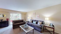 This single-floor residence offers a well-organized layout that balances comfort and functionality across its main living areas. The living room serves as the central gathering space, featuring neutral, warm-toned walls, plush carpeting, and large sliding glass doors that invite abundant natural light and provide direct access to an outdoor area with views of surrounding greenery. The open, airy feel of the room is enhanced by its generous proportions, accommodating multiple seating arrangements with ease.

The kitchen is equipped with warm wood cabinetry extending to the upper walls, dark granite-style countertops, and white appliances including a gas range, dishwasher, and refrigerator. Light tile flooring keeps the space bright and easy to maintain. Ample cabinet storage ensures practical organization throughout.

The residence includes two bedrooms, both finished with soft carpeting. The primary bedroom features a natural light-filled window with blinds and generous closet space with louvered bifold doors. A second bedroom provides additional closet storage and a calm, neutral palette.

The bathroom is finished with classic white subway tile, a gray vanity with under-sink storage, patterned floor tile, and a mirror above the sink, creating a clean and timeless aesthetic.