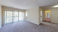 Located at 13801 Castle Blvd in Silver Spring, Maryland, this single-floor unit offers a well-organized layout designed for comfortable everyday living. The open living area is finished with neutral-toned carpet and crown molding, creating a clean, understated aesthetic. Large sliding glass doors with vertical blinds allow generous natural light to fill the space while providing access to an outdoor area and views of surrounding greenery.

The galley-style kitchen is outfitted with white cabinetry accented by chrome hardware, dark laminate countertops, wood-look vinyl flooring, and white appliances including a gas range and refrigerator. Crown molding carries through the kitchen, maintaining a consistent finish. A passthrough connects the kitchen to an adjacent carpeted area, adding functional flow to the layout.

The bedrooms are comfortably sized, each featuring plush carpet, neutral walls, and windows with vertical blinds that bring in natural light and outdoor views. The bathroom is finished with wood-look vinyl flooring, a tiled tub and shower surround, chrome fixtures, and clean white walls. Raised-panel interior doors are featured throughout, contributing to a cohesive and tidy overall presentation.